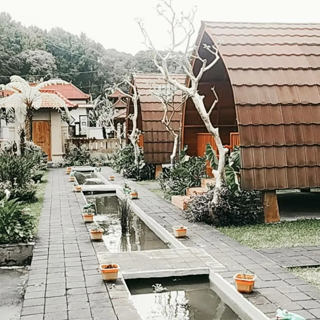 Lumbung cottages, frangipani trees and potted plants beside a stone water channel