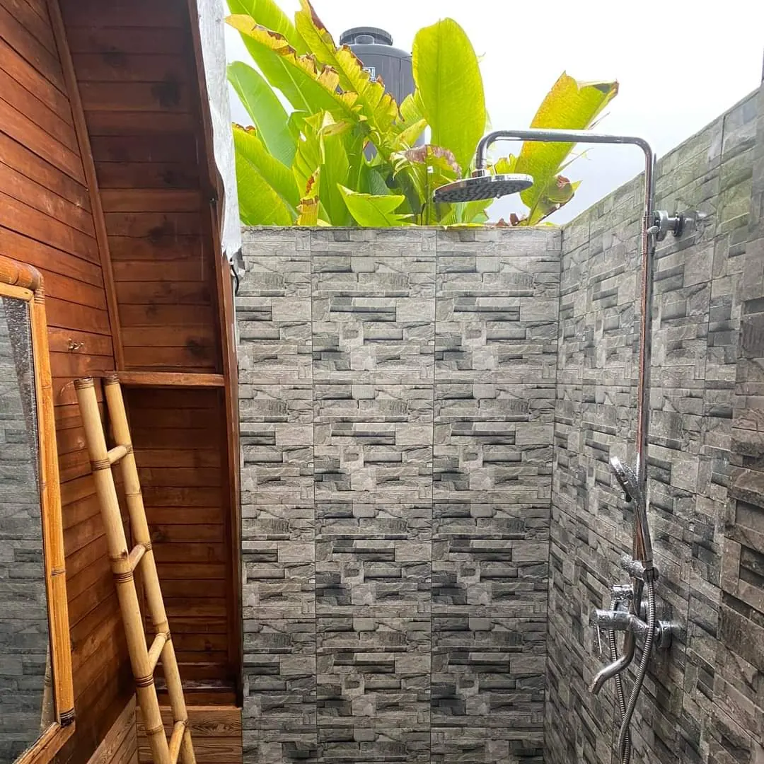 Open-air shower with stone walls, a rain shower head and a bamboo ladder towel rail